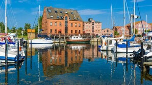 Ein Yachthafen mit vertäuten Booten, ein großes Backsteingebäude mit zahlreichen Fenstern und ein klarer, blauer Himmel.