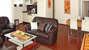 Ein modernes Wohnzimmer mit einem braunen Ledersofa, einem Glastisch und einem Essbereich mit weißen Stühlen.
