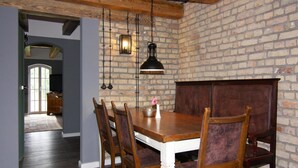 A dining area with a wooden table and chairs, a brick wall, and hanging pendant lights. - Holiday Home Birgit, Wendorf (Kuhlen-Wendorf)