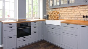 A kitchen with white cabinets, a brick wall, and a wooden ceiling. - Holiday Home Birgit, Wendorf (Kuhlen-Wendorf)