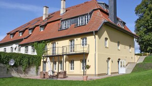 A large, yellow building with a red-tiled roof, multiple chimneys, and a balcony with outdoor furniture. - Holiday Home Birgit, Wendorf (Kuhlen-Wendorf)