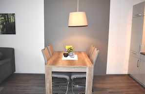 Een eetgedeelte met een houten tafel, zes stoelen, een hanglamp en een kleine plant in pot.