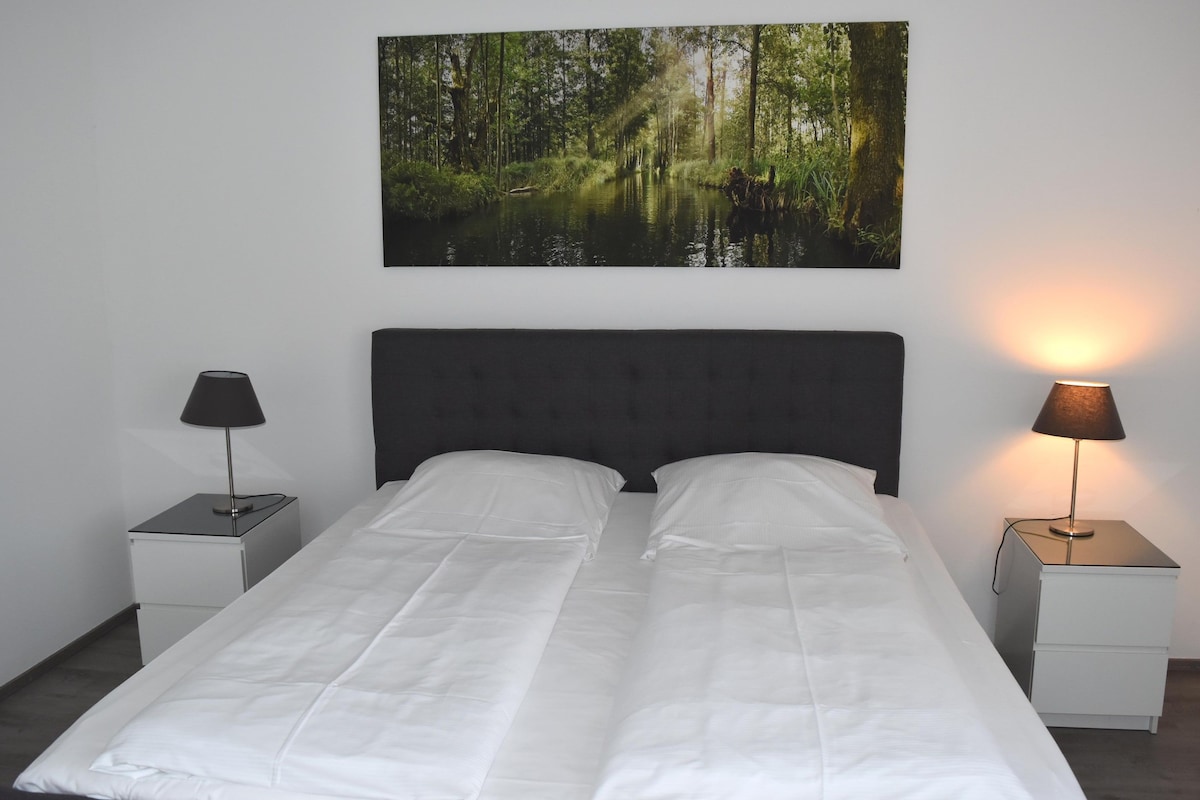 A bed with white bedding, two bedside tables with lamps, and a forest-themed wall hanging.