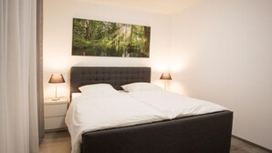 Ein modernes Schlafzimmer mit einem großen Bett, zwei Nachttischen mit Lampen und einem Wandbild mit Waldmotiv.