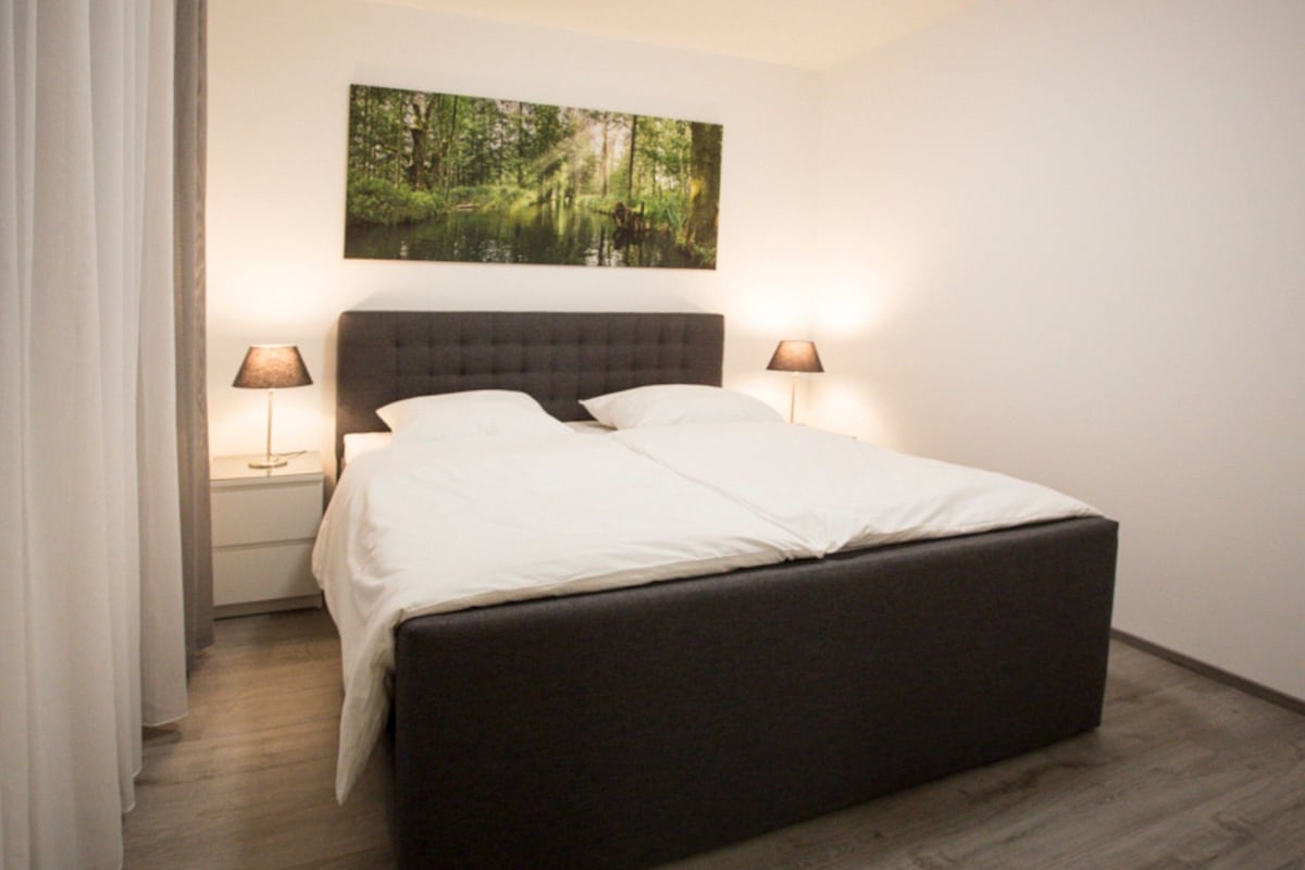 Une chambre moderne avec un grand lit, deux tables de chevet et un tableau accroché au mur.