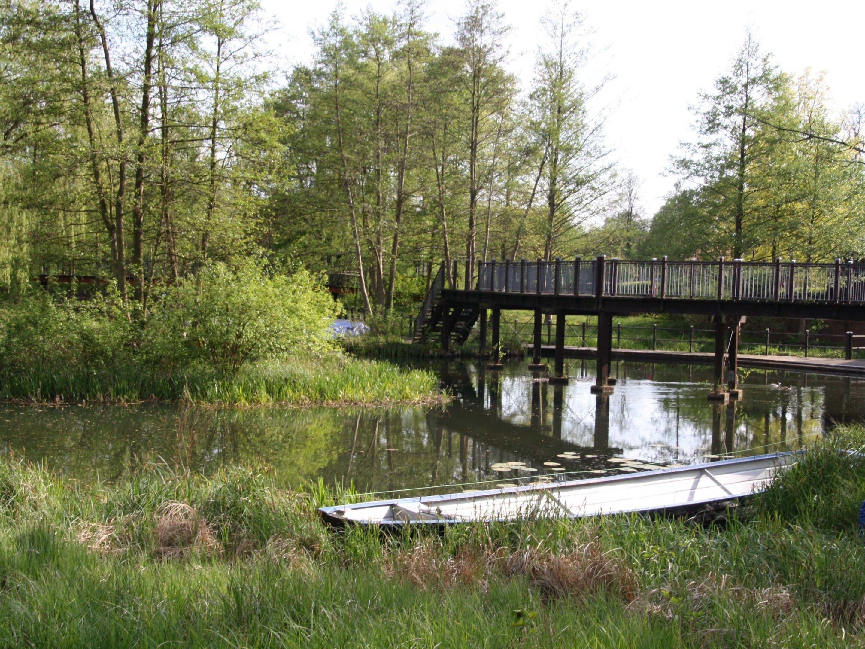 Un puente de madera sobre un río tranquilo con un bote amarrado en la orilla.