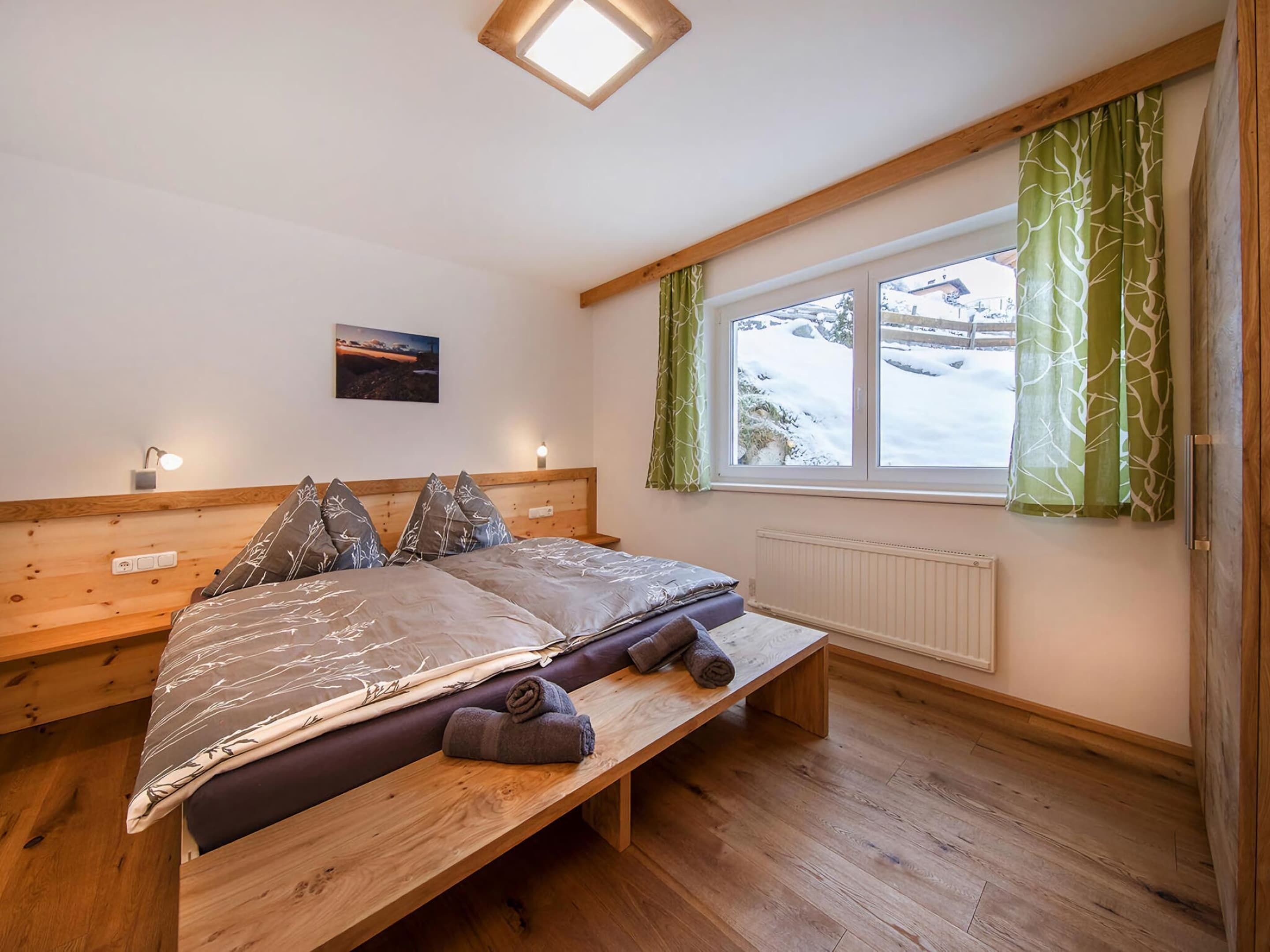 Une chambre à coucher avec un lit en bois, un banc, une fenêtre avec des rideaux et une lampe fixée au mur.