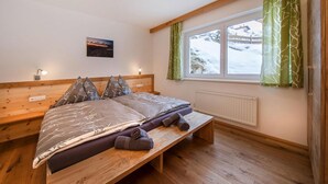 Une chambre à coucher avec un lit en bois, un banc, une fenêtre avec des rideaux et une lampe fixée au mur.
