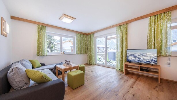 Un salon moderne avec un canapé, un pouf et un téléviseur à écran plat.