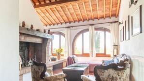 Un salón acogedor con chimenea, sillones estampados y un amplio ventanal con cortinas.