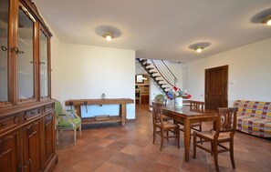 Amplia sala de estar con mesa de comedor de madera, sillas, sofá y una escalera que conduce a un piso superior.