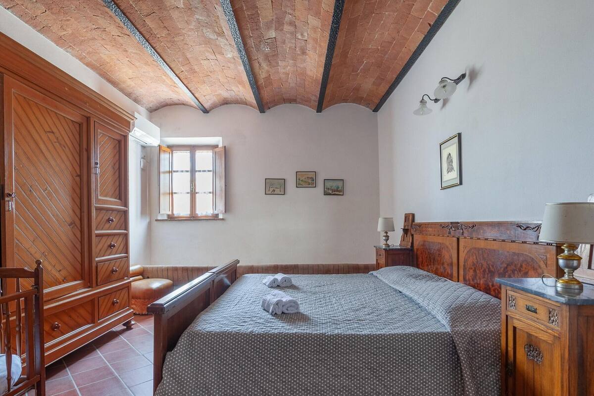 A bedroom with a wooden bed, a nightstand, a wardrobe, and a window with curtains.