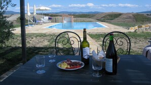 Una mesa con un plato de comida, dos botellas de vino y copas, con vistas a una piscina y colinas.