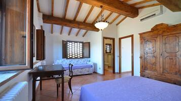 A bedroom with a bed, a wooden wardrobe, a table with a chair, a window with blinds, and a ceiling fan.