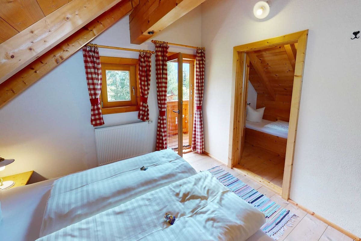 A cozy attic bedroom with a bed, a window with checkered curtains, and a wooden loft bed.