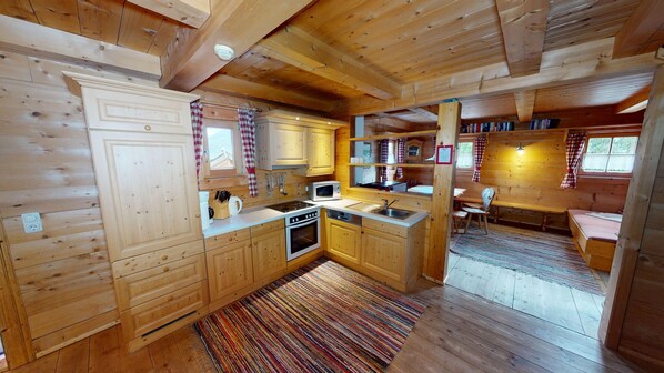 A cabin-style kitchen with wooden cabinets, a microwave, stove, and a sink. - Chalet in Neukirchen (Neukirchen am Grossvenediger)