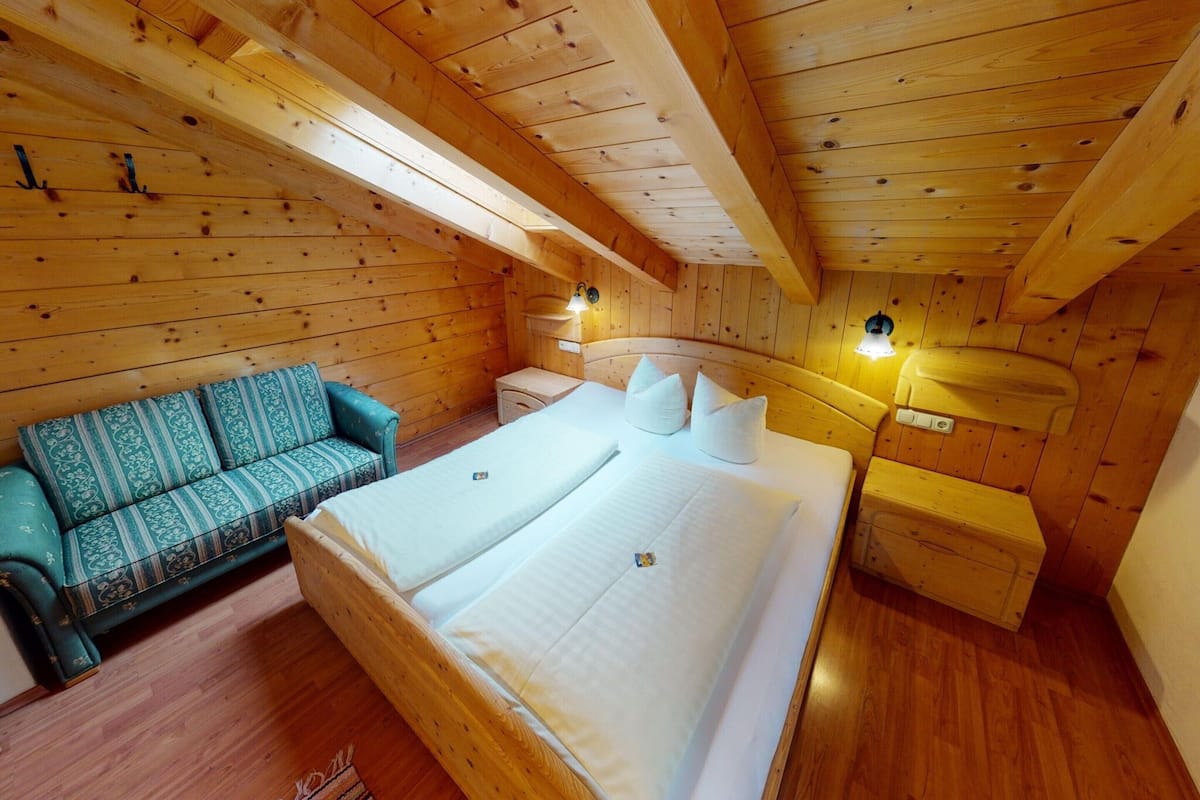 A wooden cabin bedroom with a bed, a sofa, and a chest of drawers.