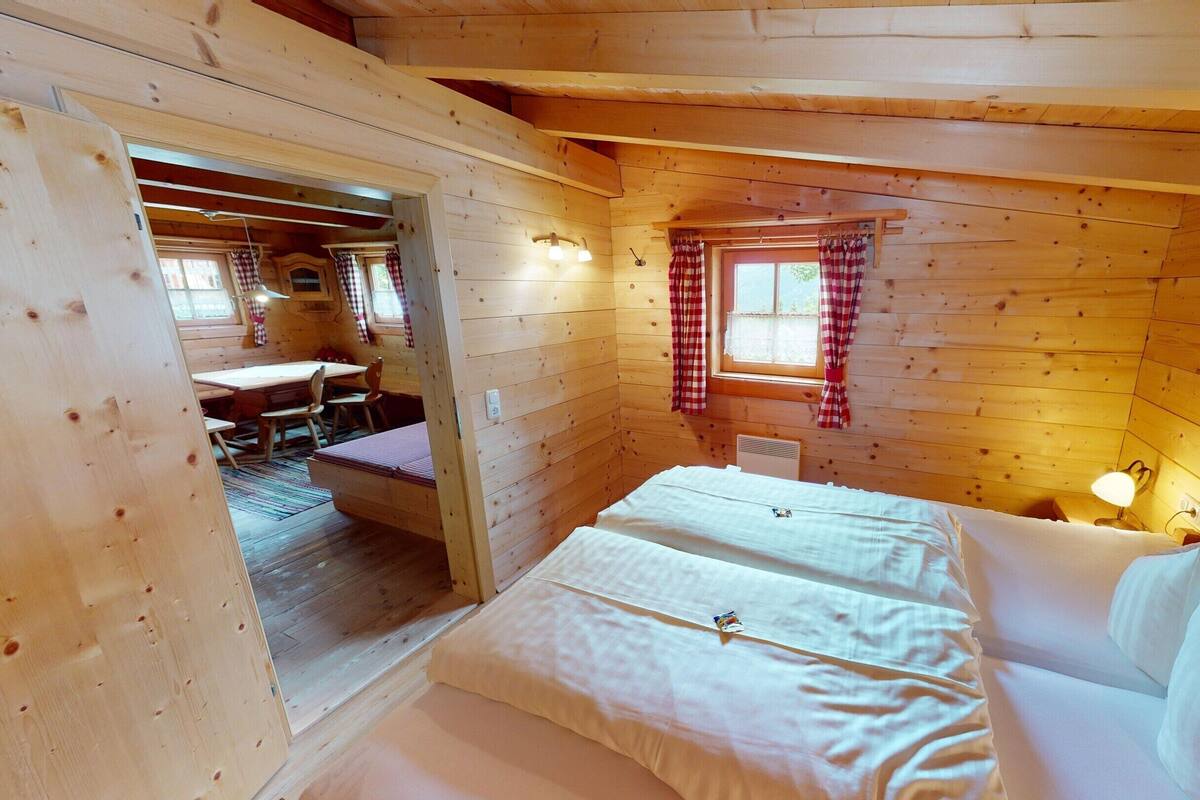 A cozy wooden cabin room with a bed, a window with curtains, and a small table with chairs.