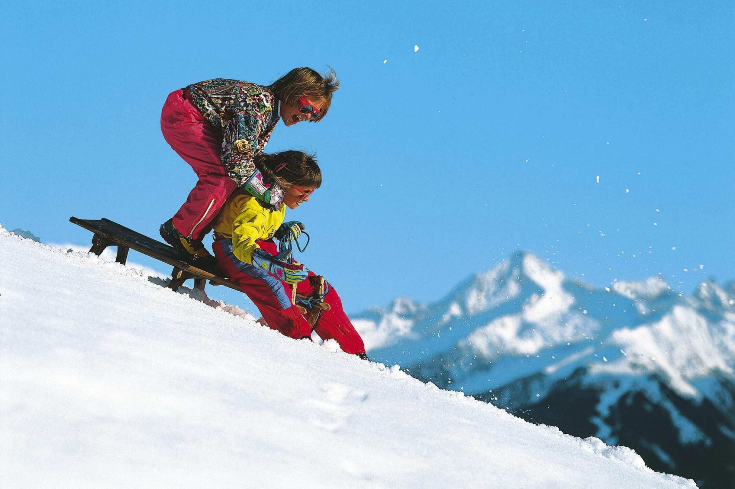 A snowy mountain slope with a person in a yellow jacket and red pants sliding down.