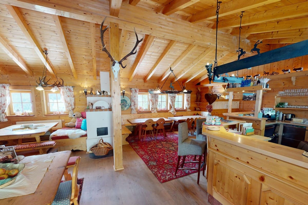 A rustic wooden cabin interior with a dining area, kitchen, and a large window.