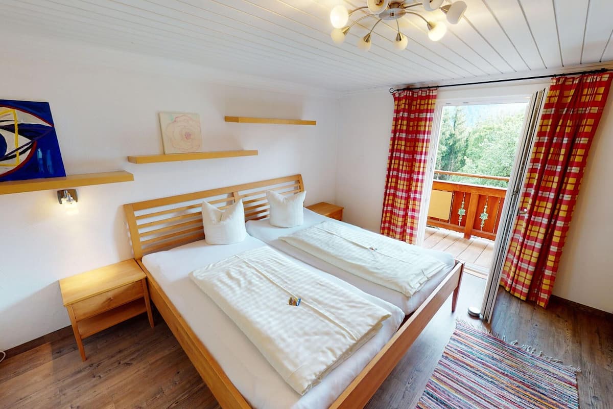 A bedroom with a wooden bed, bedside tables, a ceiling light fixture, and a balcony with red and yellow checkered curtains.