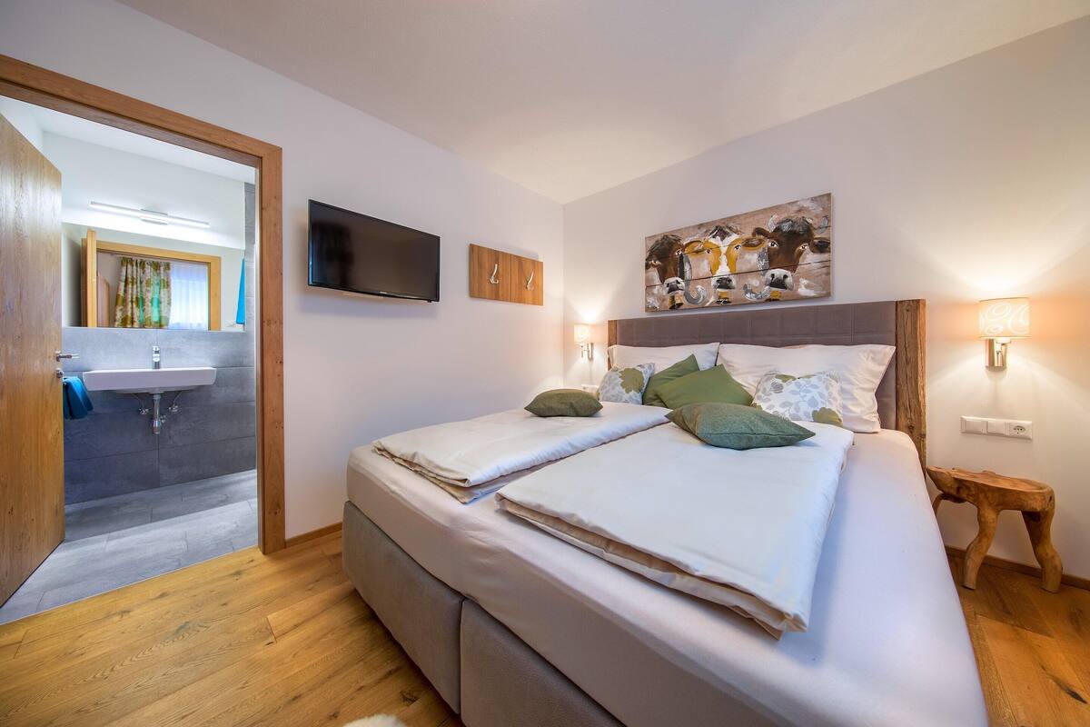 A bedroom with a bed, a TV, a painting, and a bedside lamp.