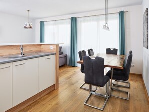 A modern kitchen with a wooden countertop, a sink, and a dining area with a table and chairs. - Apartment in the Heart of Neukirchen (Neukirchen am Grossvenediger)