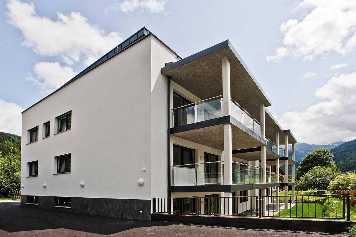 Een modern gebouw met een plat dak, grote ramen en een balkon met glazen balustrades.