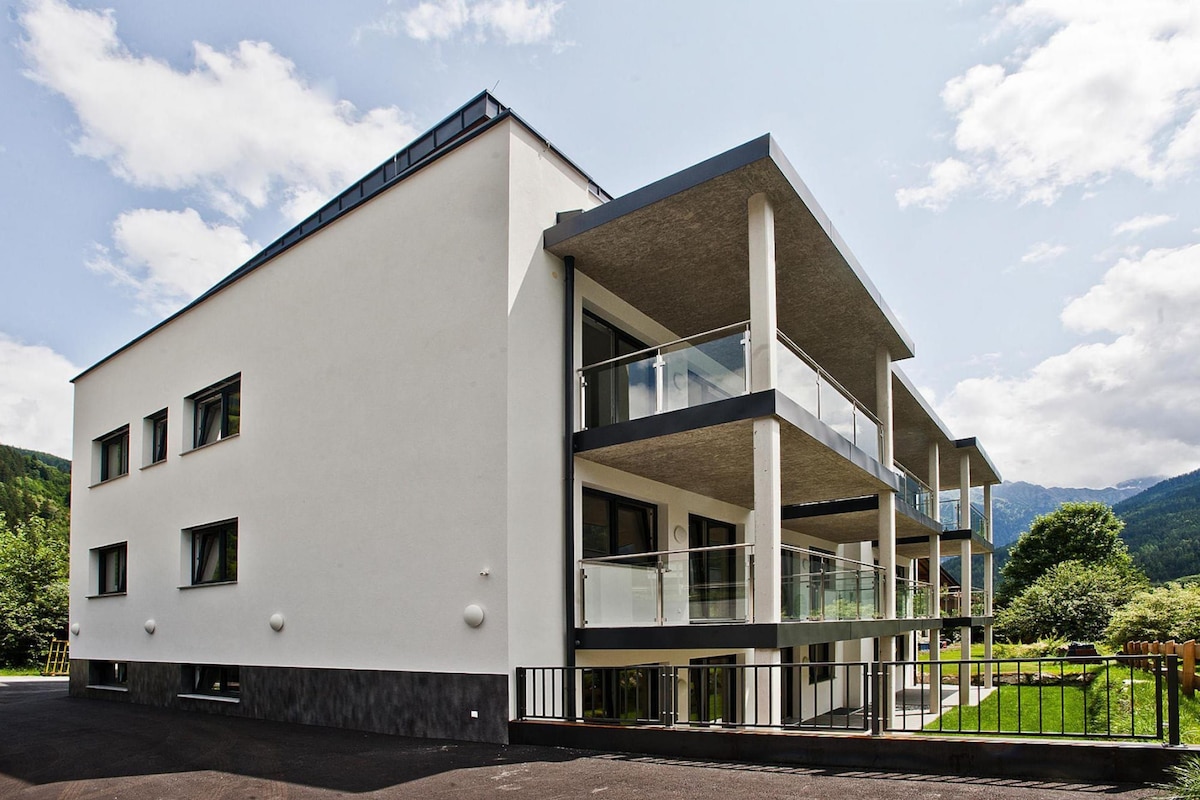A modern building with a flat roof, large windows, and a balcony with glass railings.
