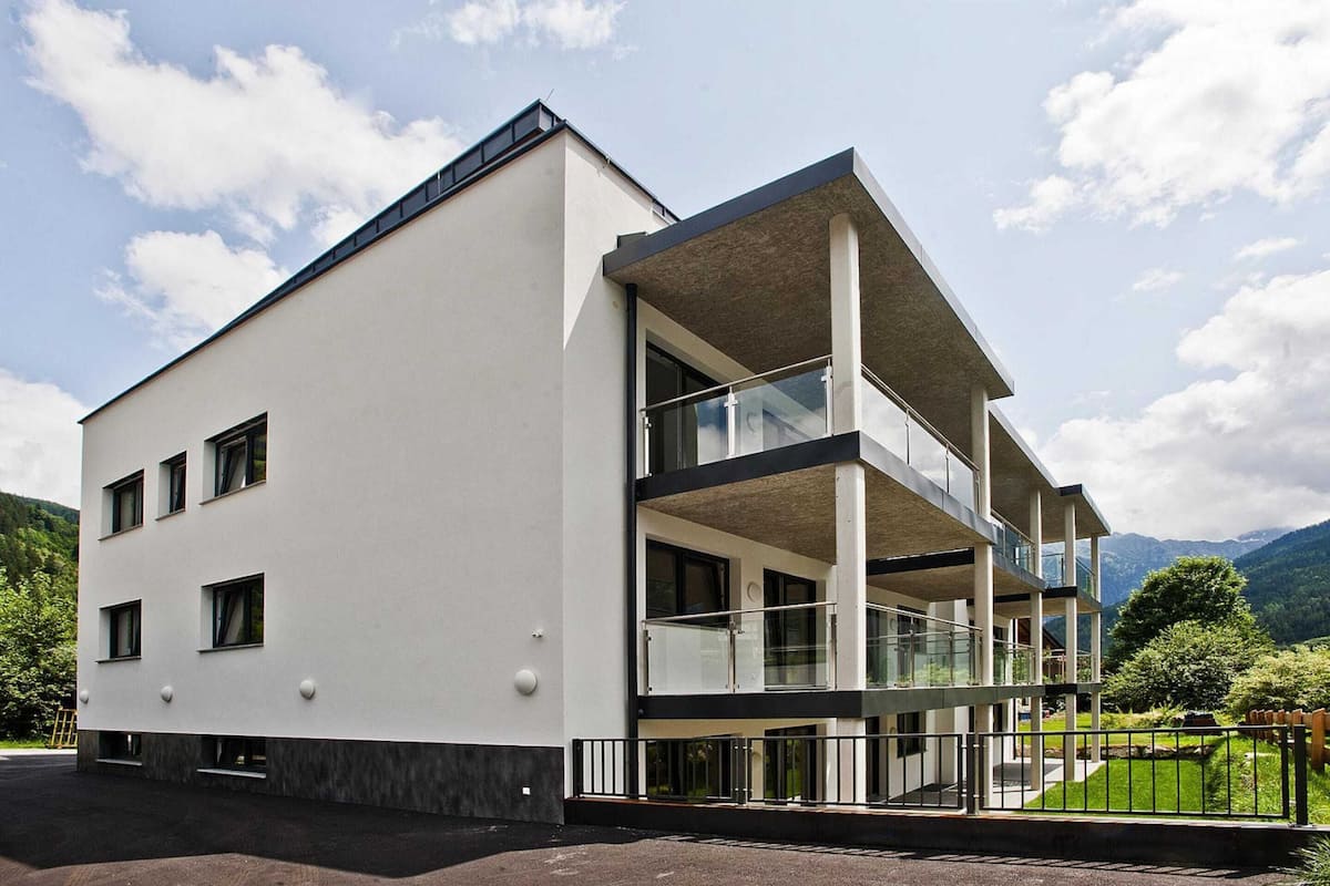 Un bâtiment moderne doté d’un toit plat, de grandes fenêtres et d’un balcon avec des garde-corps en verre.