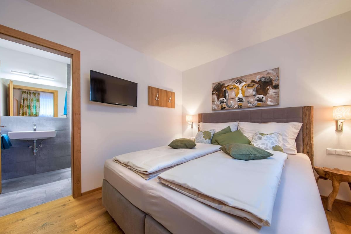 A modern bedroom with a large bed, a flat-screen TV, a wooden headboard, and a painting on the wall.