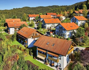Ein Wohngebiet mit Häusern, die rote Ziegeldächer und weiße Wände haben, umgeben von Grünflächen und Hügeln.