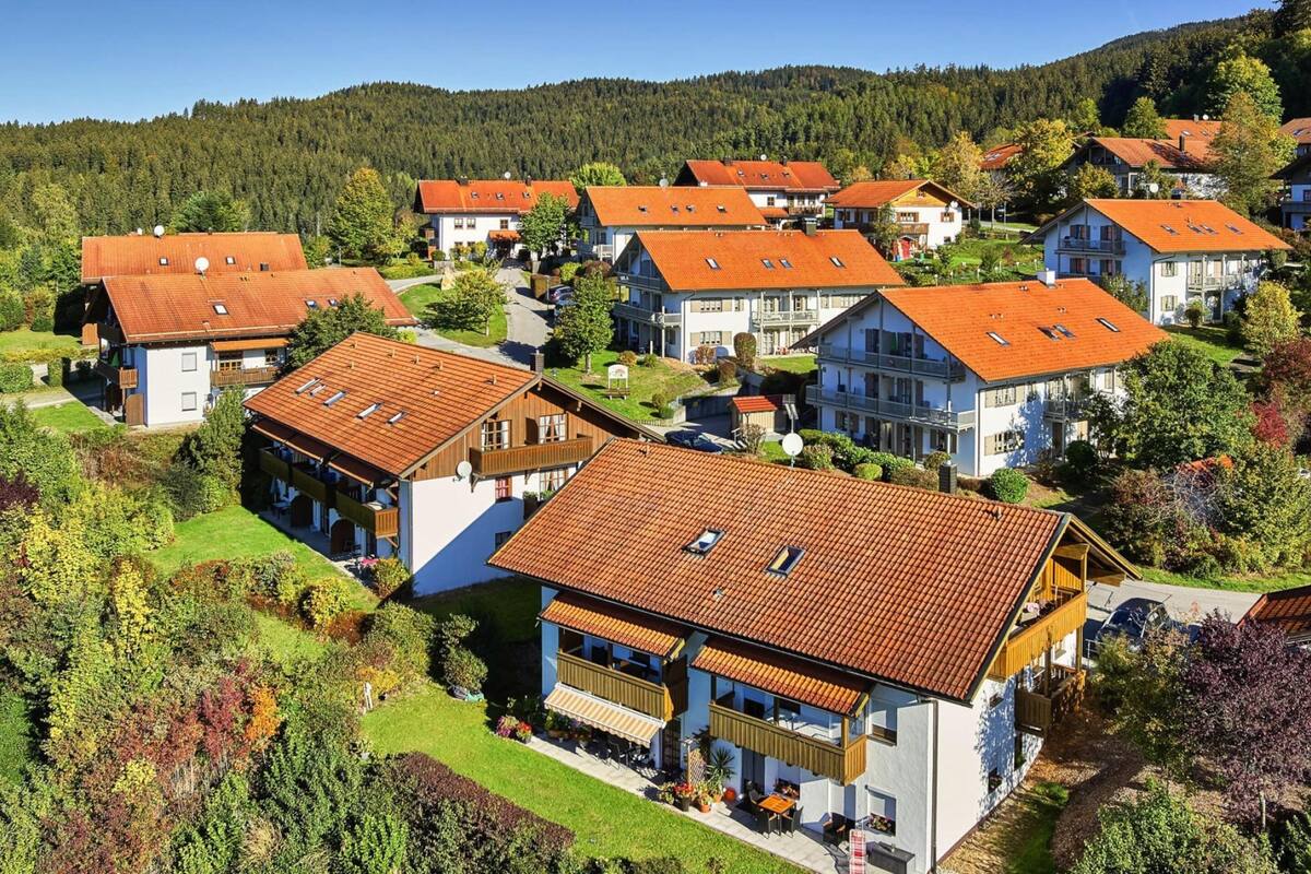 A residential area with houses featuring red-tiled roofs and white walls, surrounded by greenery and hills.