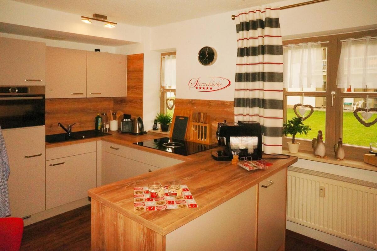 A modern kitchen with wooden cabinets, a central island, and a window with heart-shaped decorations.