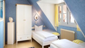 A bedroom with a sloped ceiling, a white wardrobe, a bed with white bedding, a small table, and a radiator. - Apartments Haus Burgund, Meersburg (Meersburg)