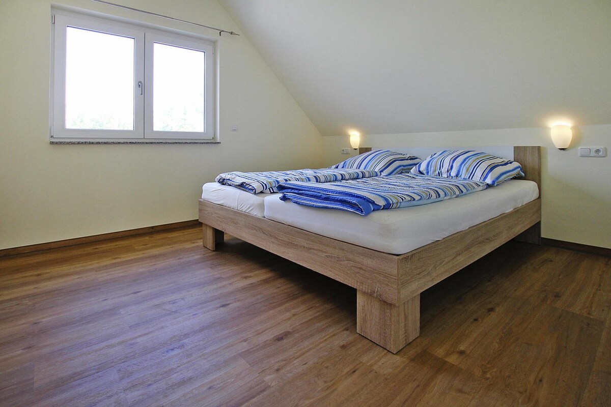 A bedroom with a wooden bed, two bedside lamps, a window, and a sloped ceiling.