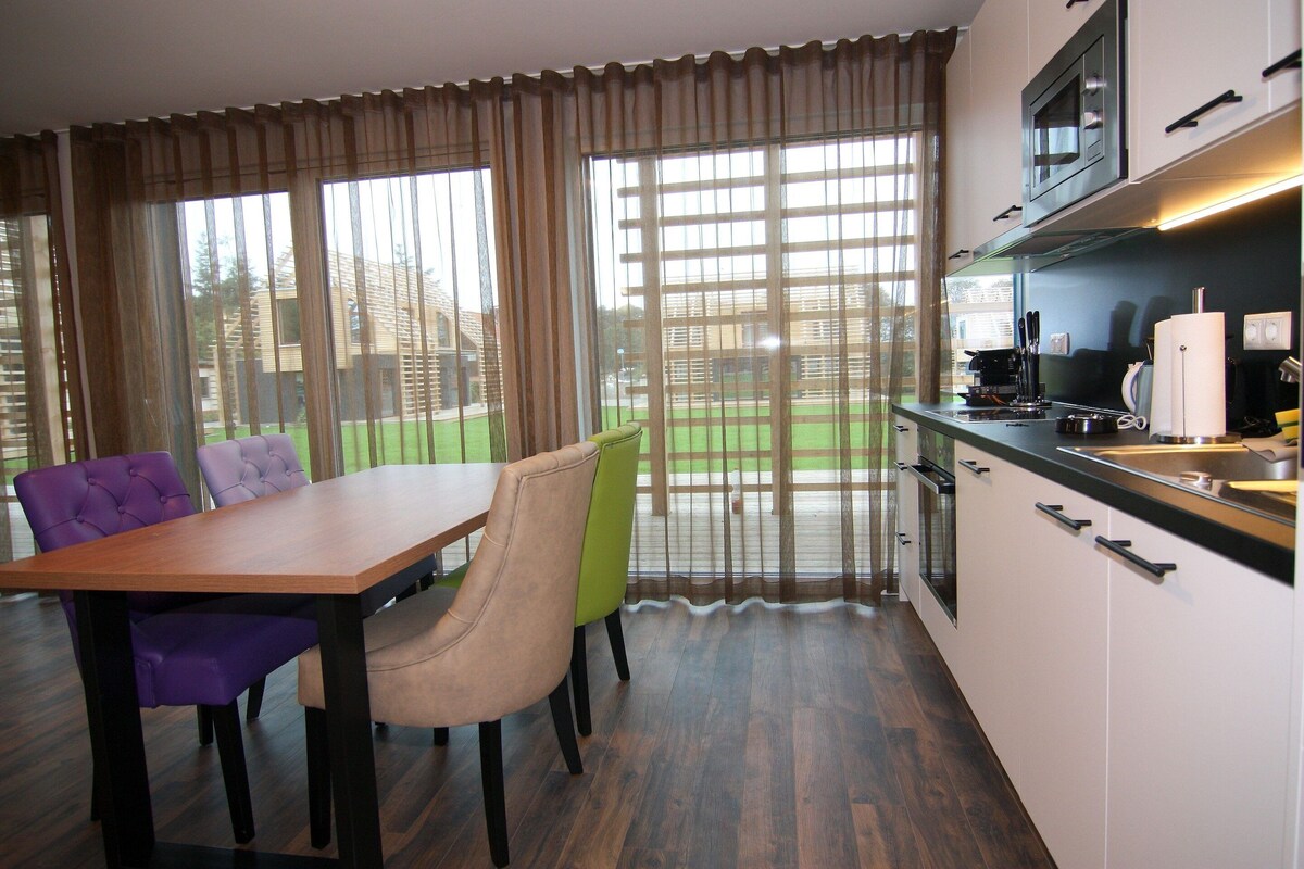 A modern kitchen with a dining area, featuring a wooden table, chairs, and a large window with curtains.