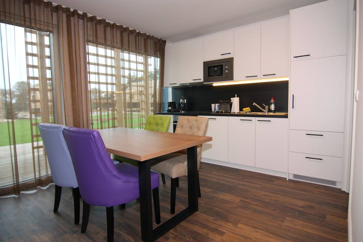A modern kitchen with white cabinets, a wooden dining table, and purple chairs.