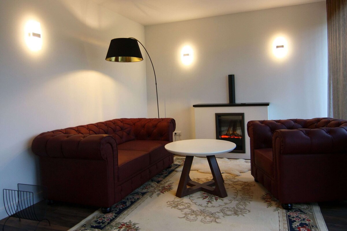 A living room with two red sofas, a white table, and a fireplace.