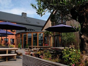 Eine Terrasseneinrichtung im Freien mit Holzbänken und Tischen, umgeben von Pflanzen und Blumen.