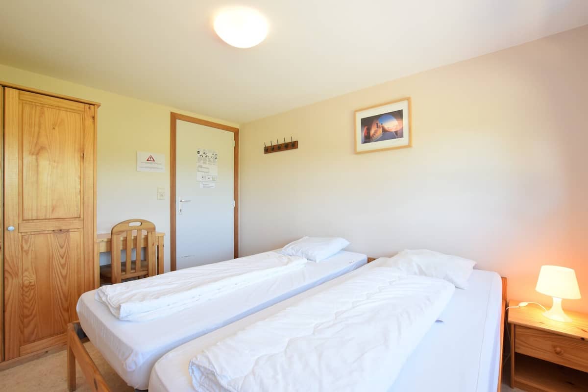 Un dormitorio con dos camas individuales, un armario de madera, un escritorio y una mesita de noche con lámpara.