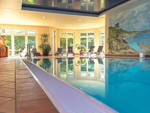 An indoor swimming pool with clear glass walls, lounge chairs, and a mural of a coastal landscape. - Seepark Heidenholz, Plau am See (Plau am See)