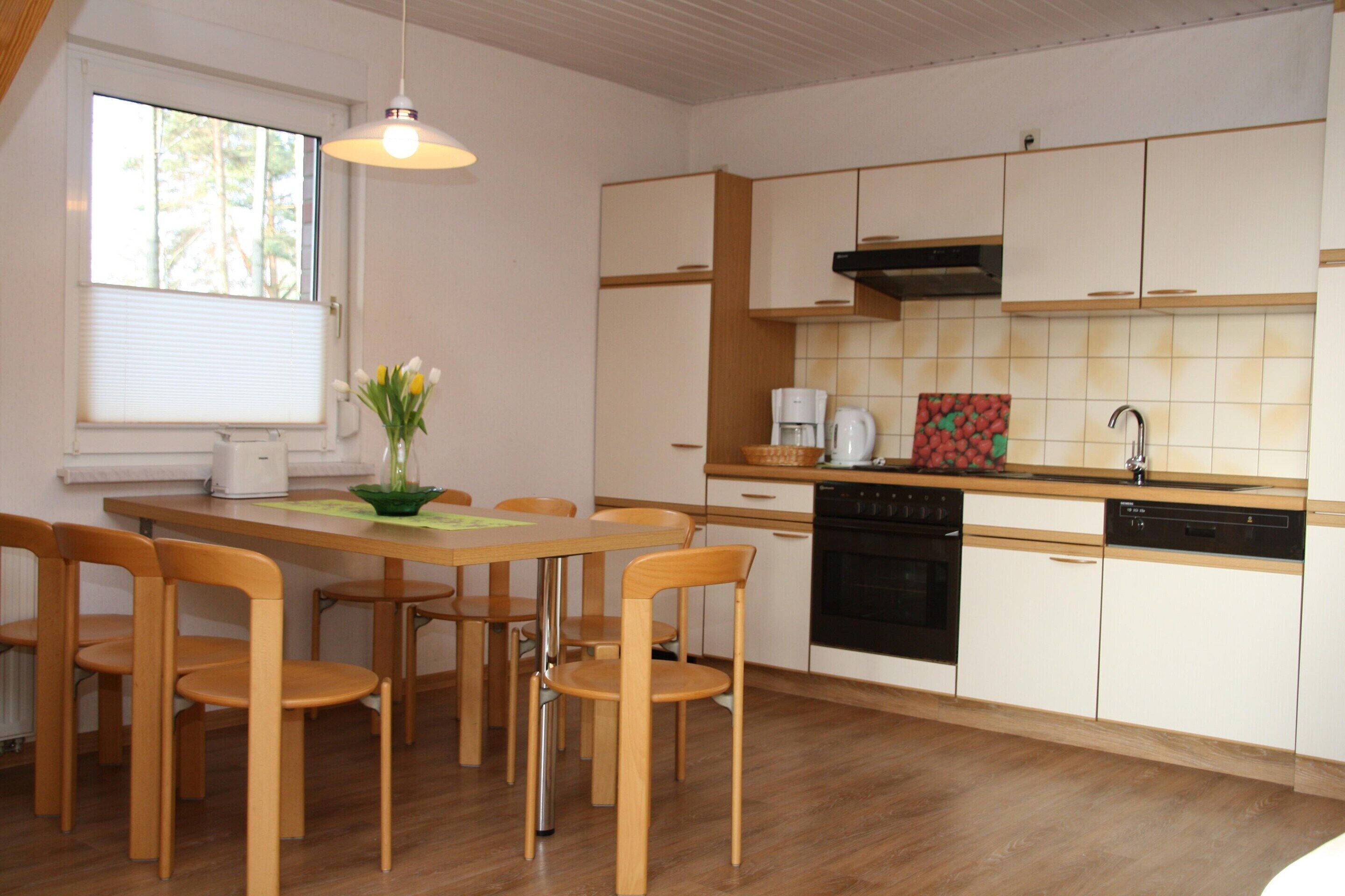 A modern kitchen with wooden cabinets, a dining table with chairs, a coffee maker, and a sink.