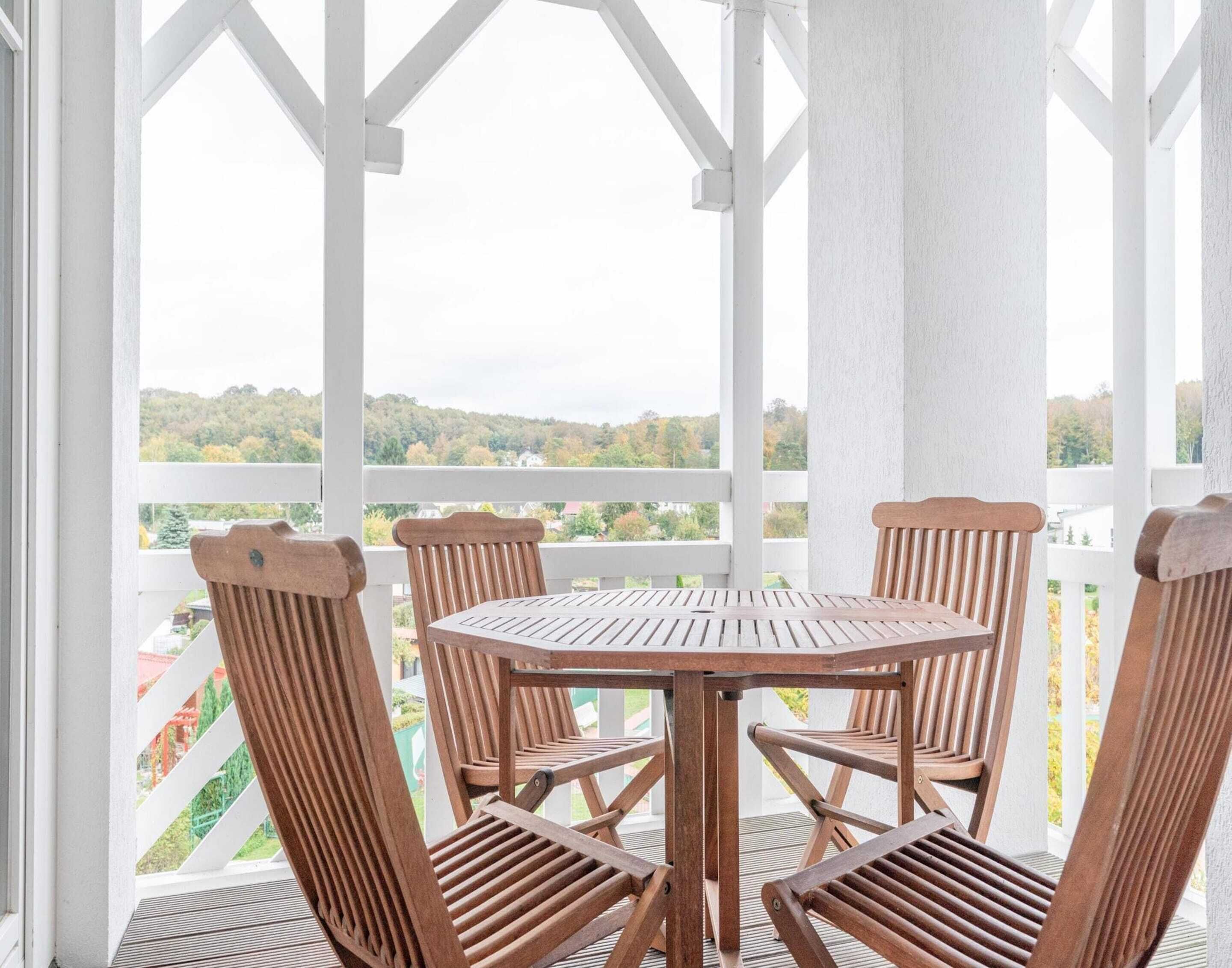 Una mesa redonda de madera con seis sillas, ubicada en un balcón con barandillas blancas y vistas a un paisaje verde.