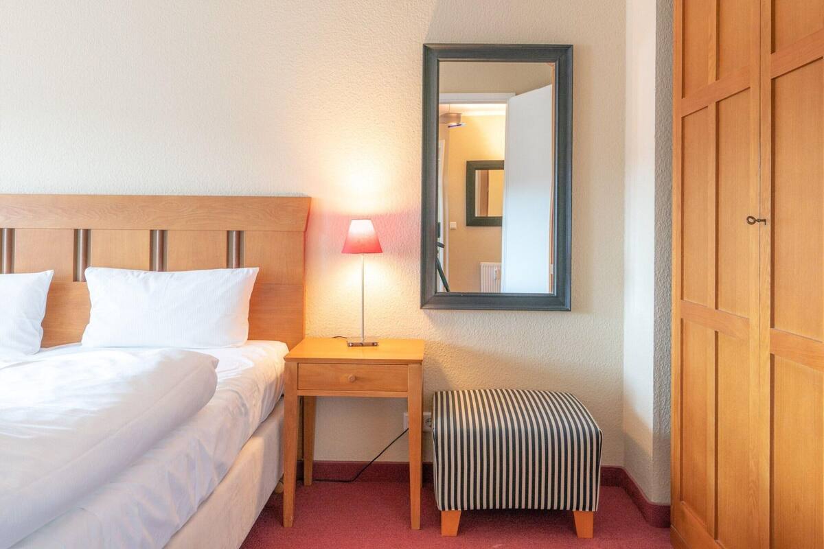 Ein Hotelzimmer mit Bett, Nachttisch, Lampe, Spiegel und Kleiderschrank.