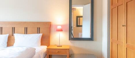 Una habitación de hotel con cama, mesita de noche, lámpara, espejo y armario.