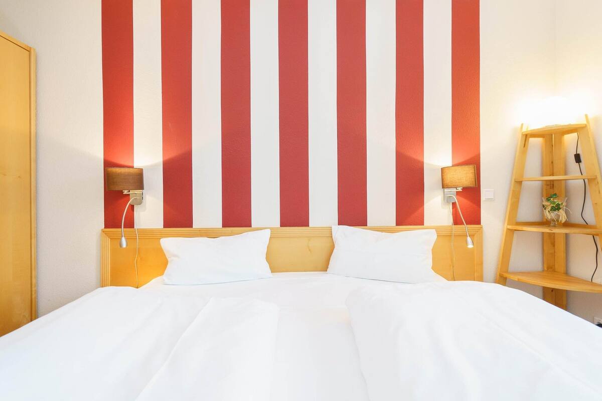Ein Hotelzimmer mit einem Bett, zwei Nachttischen mit Lampen, einem hölzernen Kopfteil und einer Wand mit roten und weißen Streifen.