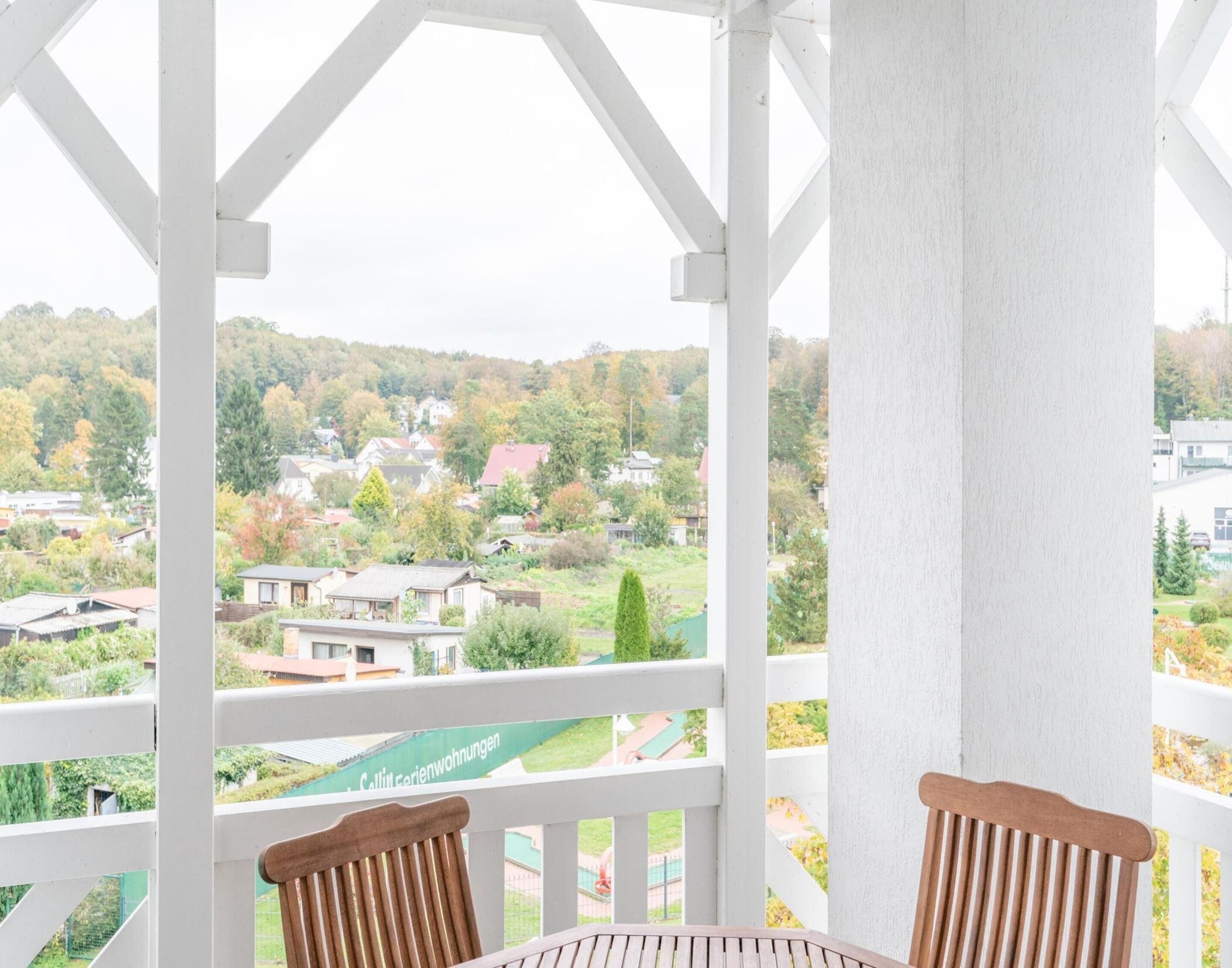 Uma varanda com vista para uma área residencial, uma cadeira de madeira e uma mesa.