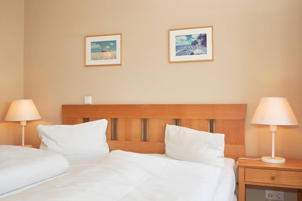 Ein Hotelzimmer mit einem Doppelbett, zwei Nachttischen mit Lampen und zwei gerahmten Bildern an der Wand.