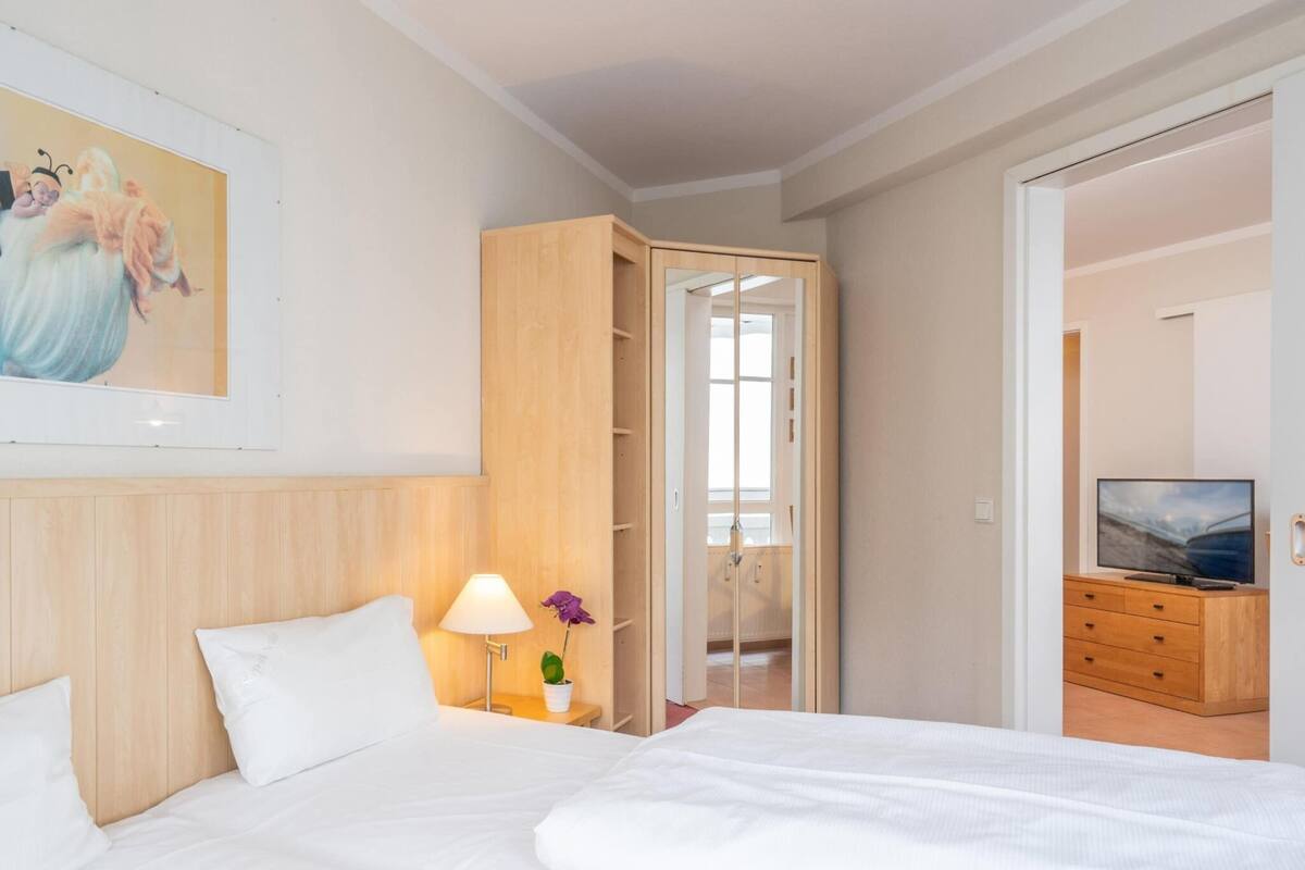 Ein Hotelzimmer mit einem Bett, einem Nachttisch mit Lampe, einem Fernseher auf einer Holzkommode und einer Tür, die in einen anderen Raum führt.